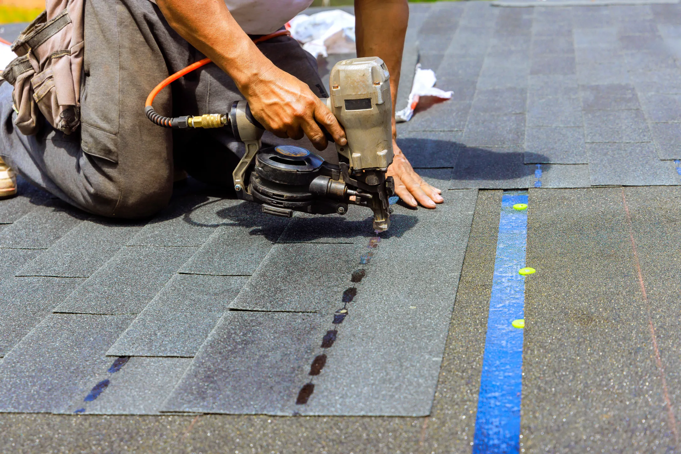 Roofer using a pneumatic nail gun with correct nailing technique during shingle roof installation.